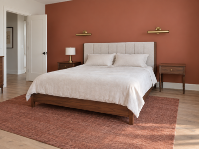 A walnut platform bed against a terracotta accent wall with brass sconces, clear walking space visible on both sides.