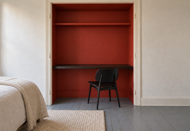 A bedroom closet painted red inside and fitted with a slim floating desk and a black wooden chair.