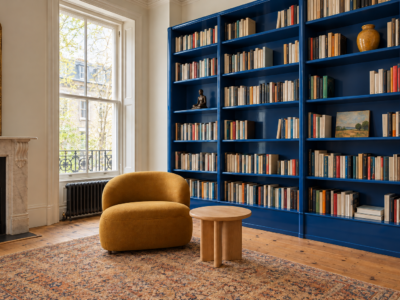 Built-in bookshelves with a glossy cobalt back, full of books and a few objects, beside an ochre lounge chair.