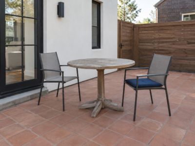 A small patio with a round teak pedestal table and two sling chairs, sized to leave clear space around it.