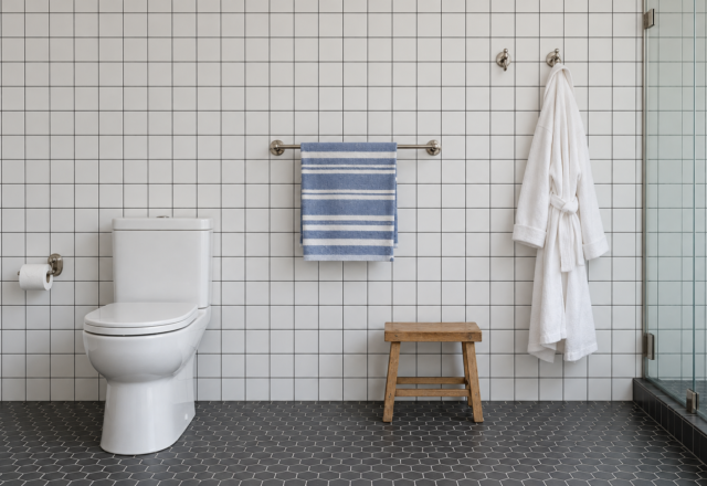 A bathroom wall of white square tile with a paper holder, a towel bar, and robe hooks mounted at different heights.