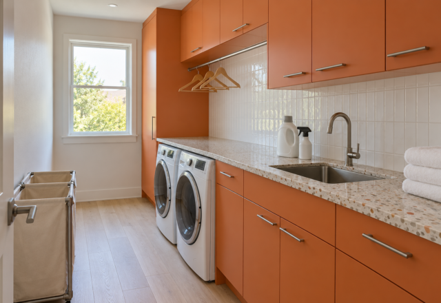 A laundry room with persimmon cabinets, front-loading machines under a terrazzo counter, and a hanging rail above.