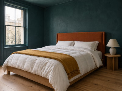 A queen bed with a lofted white comforter and an ochre throw, against deep teal walls and a rust linen headboard.