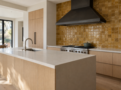 A kitchen range wall with ochre-glazed tile running from the counter to the underside of a slim black steel range hood.