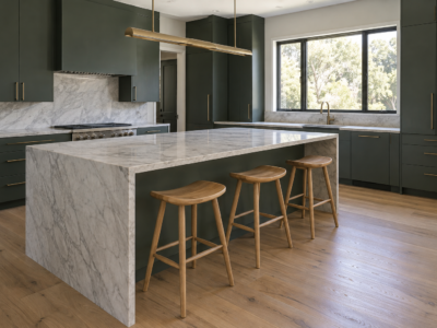 A kitchen island with a pale stone waterfall counter and three white oak saddle-seat stools sitting at a comfortable counter-height under a brass pendant.