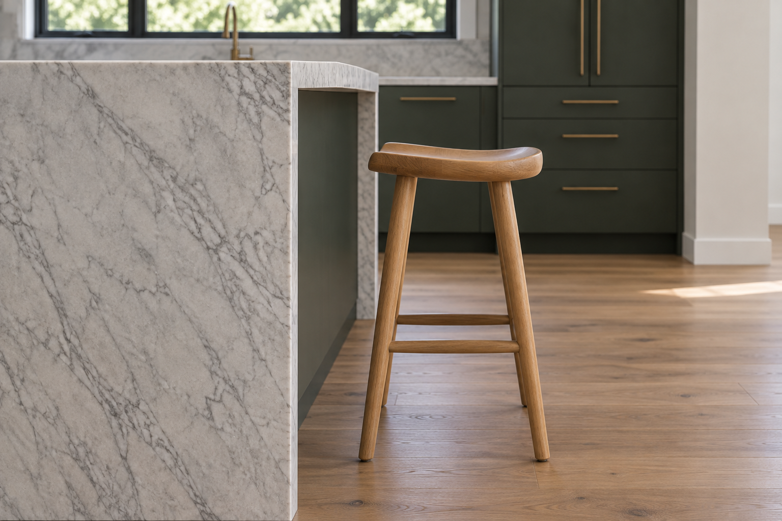 A close side profile of a white oak saddle-seat counter stool beside a kitchen island, showing the gap between the seat and the stone counter's overhang.