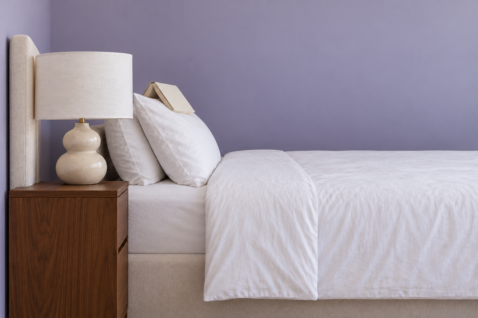 A side view of a bedside lamp whose shade bottom sits at about chin height for someone propped against the pillows.