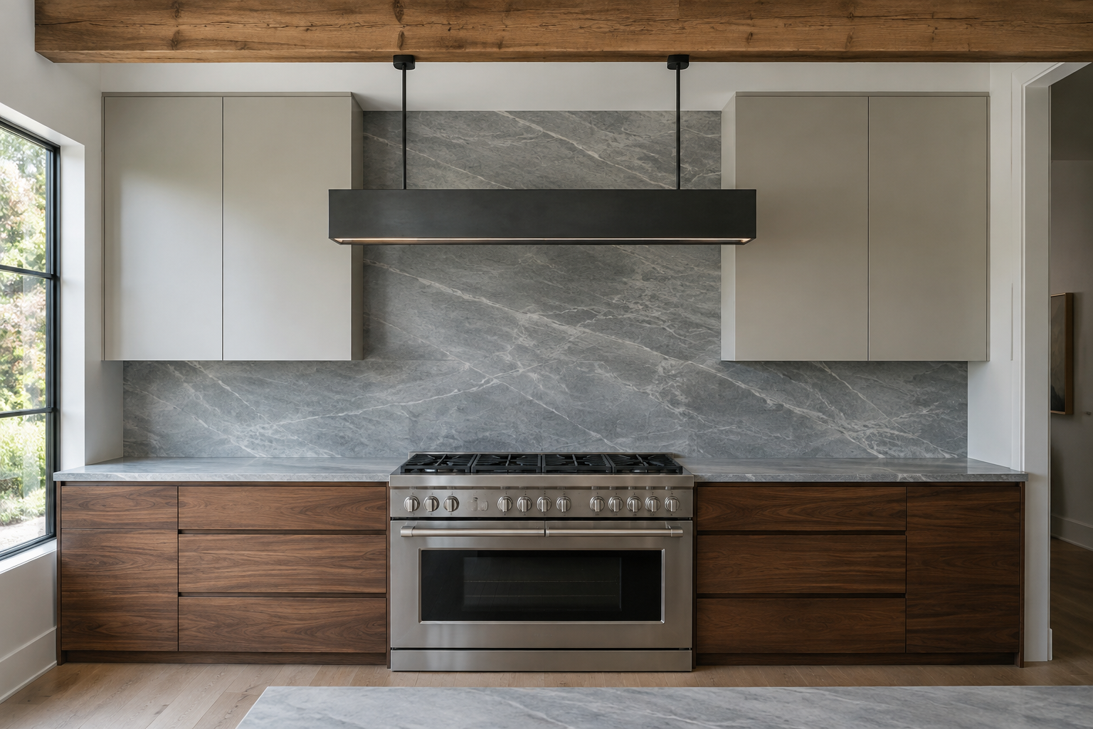 A dove-gray quartzite slab backsplash with continuous veining and no grout lines, walnut cabinetry below, exposed ceiling beam above.