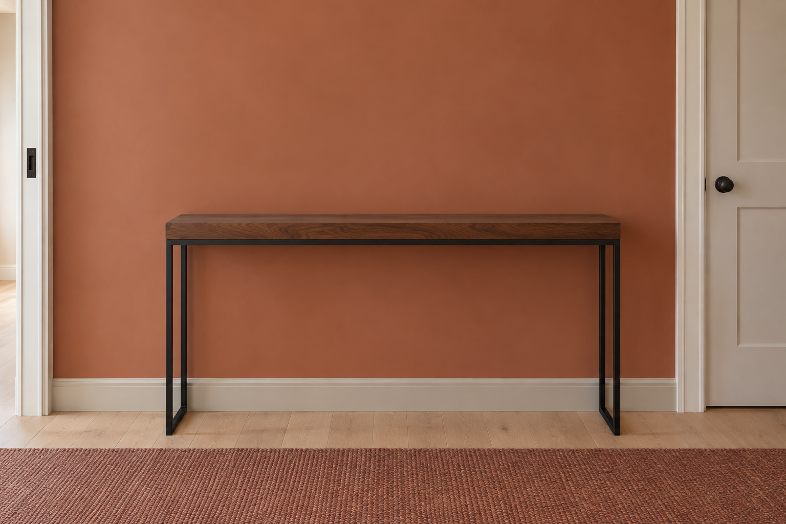 A black steel console table shown straight-on against the wall section it occupies, next to a door casing, in a narrow entry hallway.