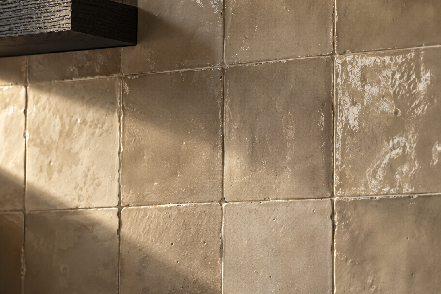Close detail of warm greige handmade zellige tile in raking light, showing natural glaze variation and irregular edges.
