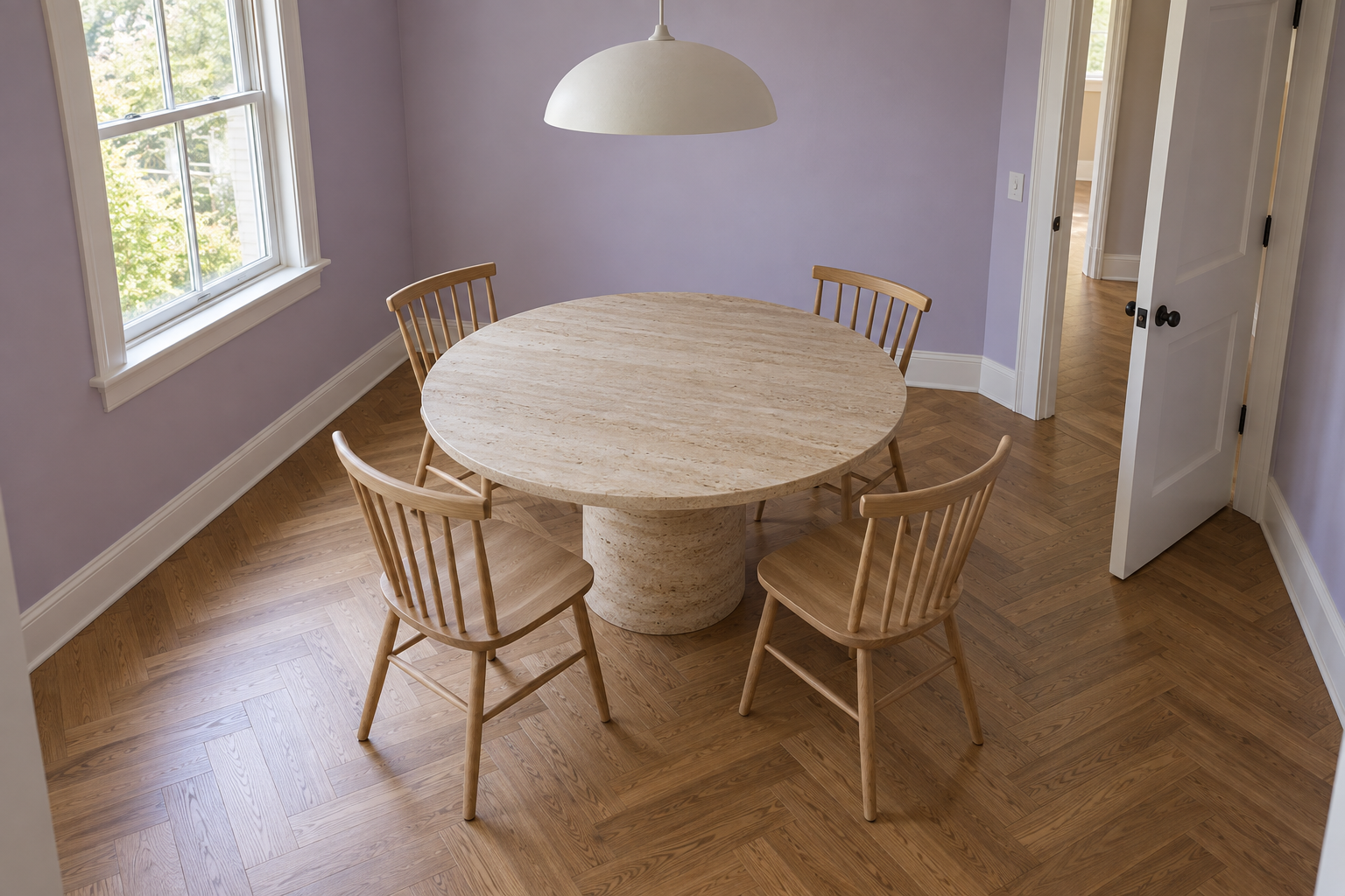 A round travertine pedestal table with four spindle-back chairs centered in a small square dining room with pale lilac walls.