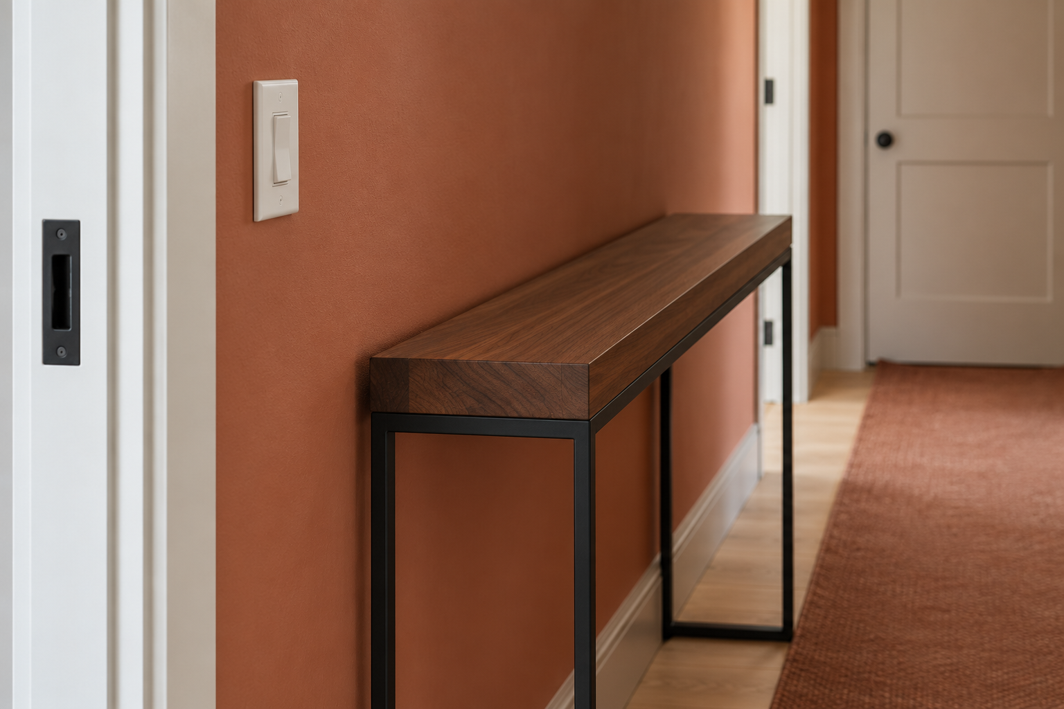 A close detail of a black steel console table's height against a standard wall light switch plate in a narrow entry hallway.