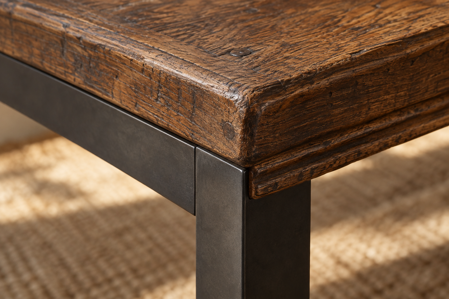 A close detail of aged carved oak meeting a blackened-steel table leg, an old material and a new one sharing one joint.