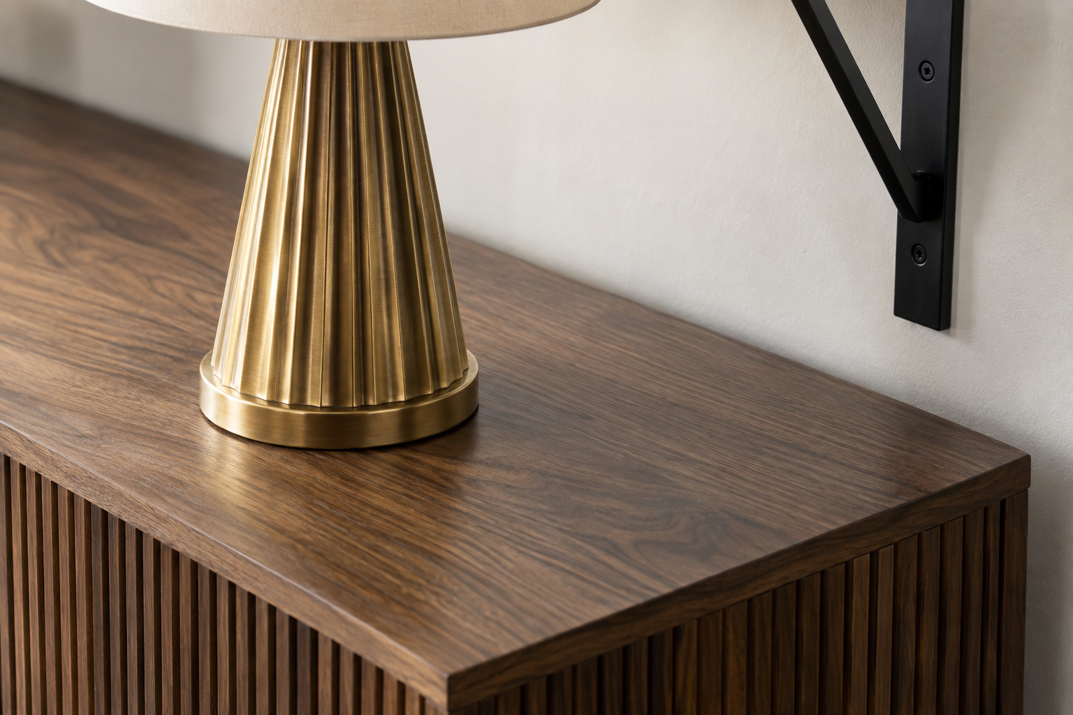 A close detail of a brass table lamp base on a reeded walnut console, with a matte black wall bracket visible nearby.