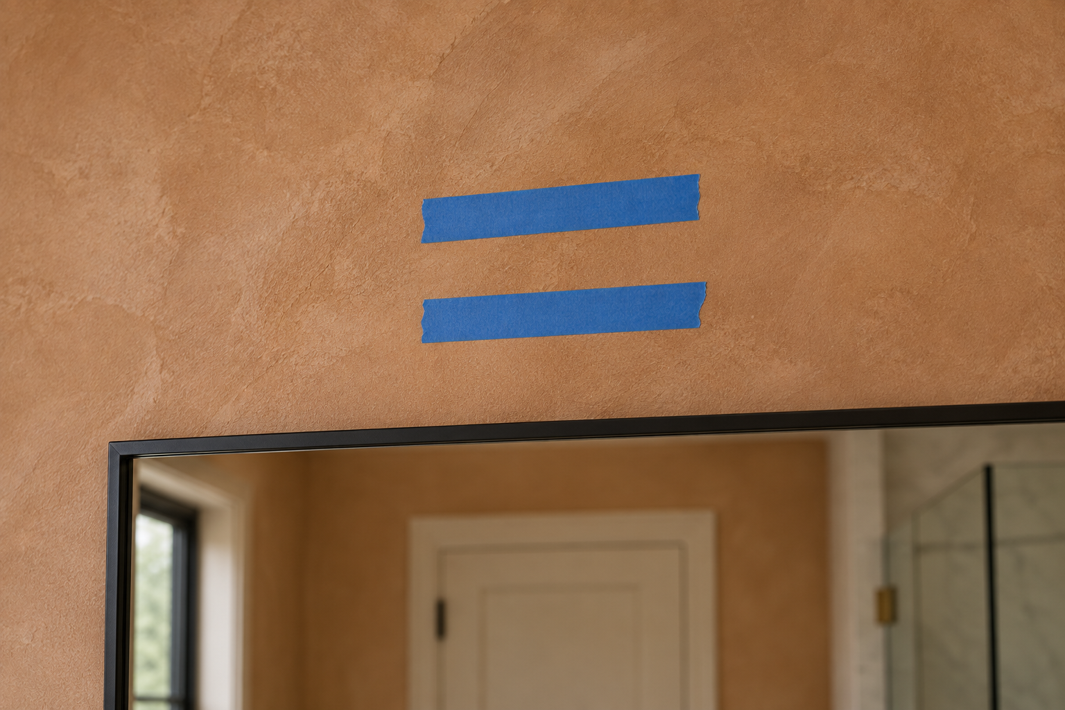 Two strips of painter's tape at different heights on a bathroom wall above a mirror, marking candidate positions for a new light fixture before installation.