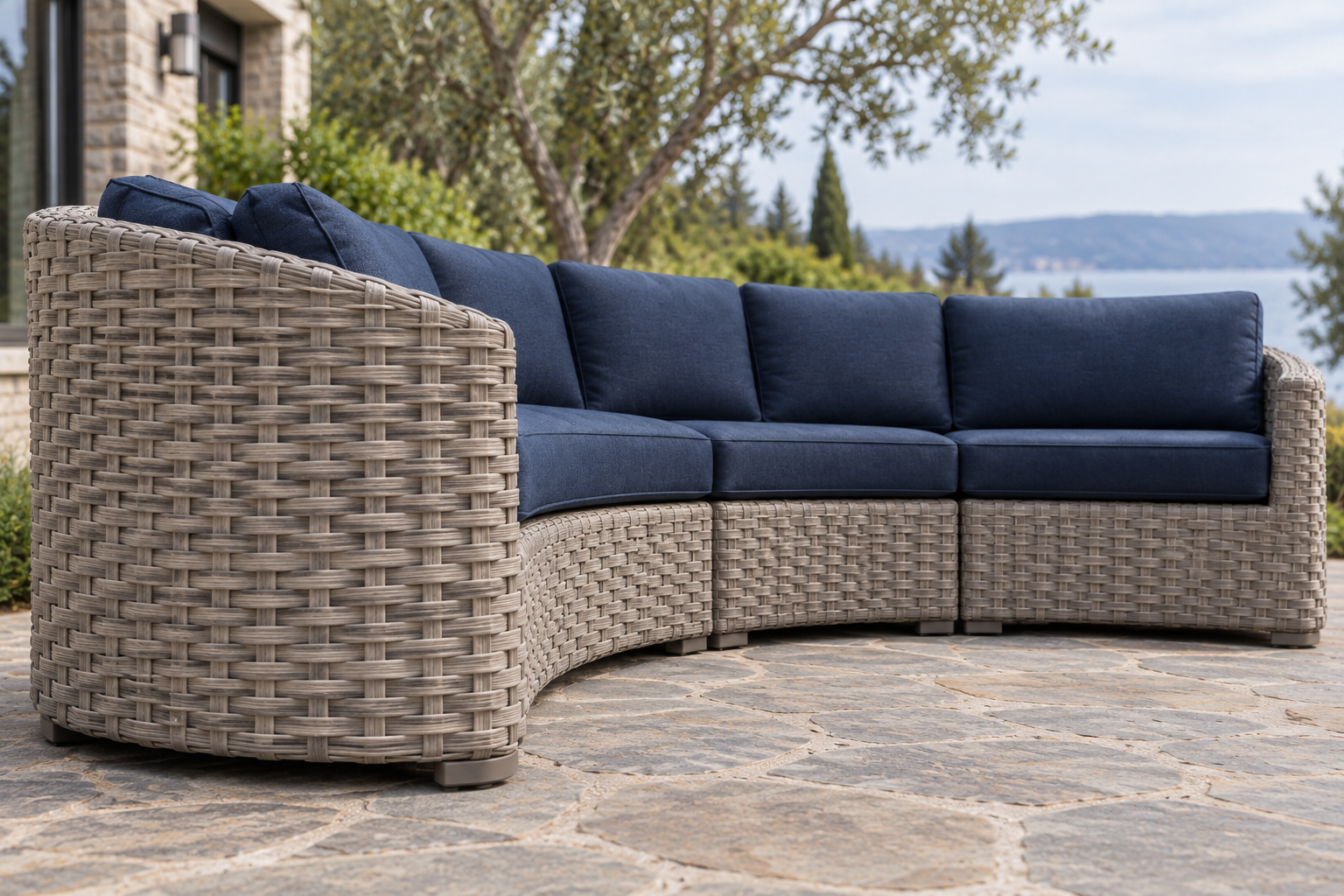 A curved barrel-form outdoor sectional woven in driftwood-gray wicker with navy cushions.