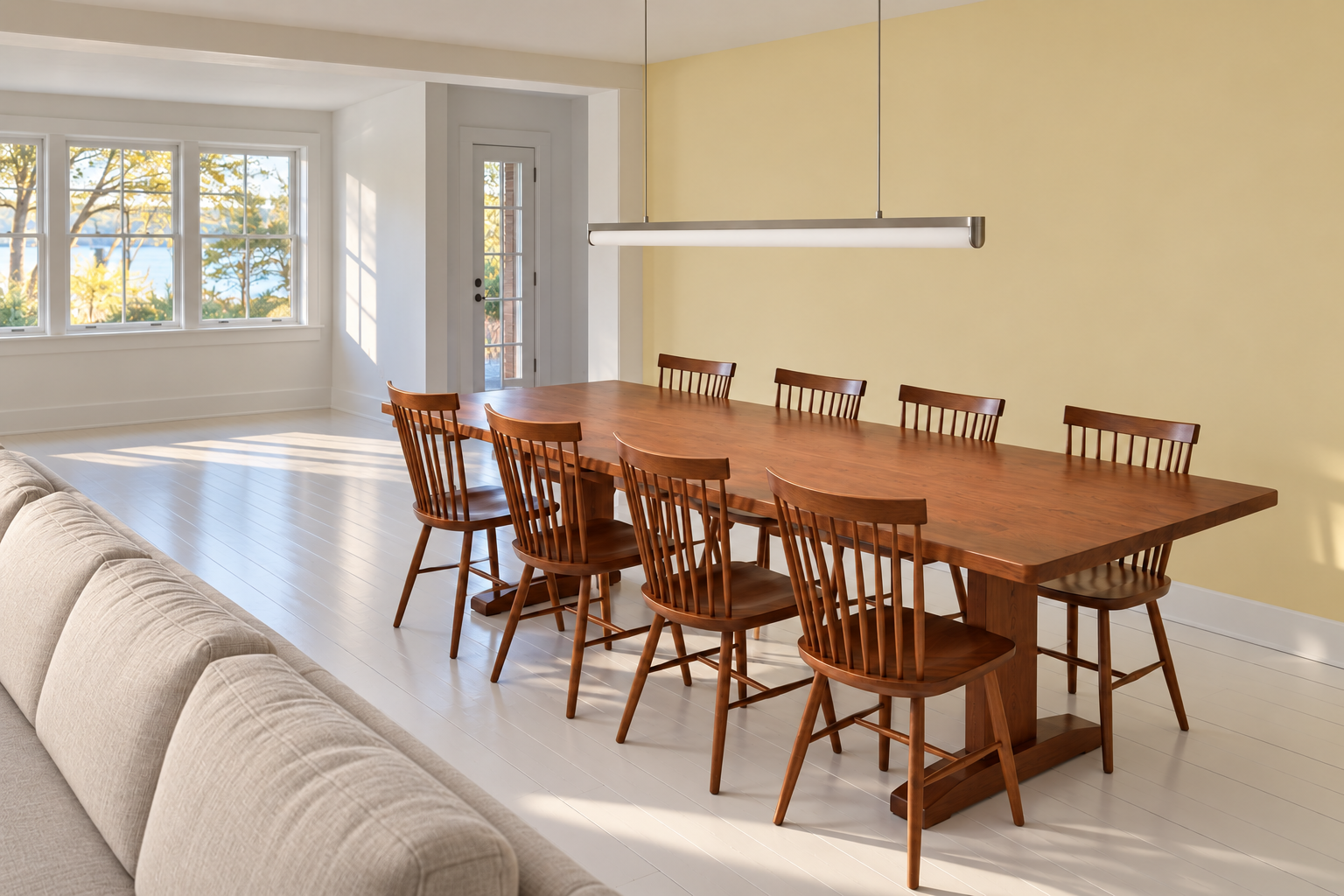 A long cherry dining table under a linear nickel light bar about two-thirds of the table's length, in an open-plan room.