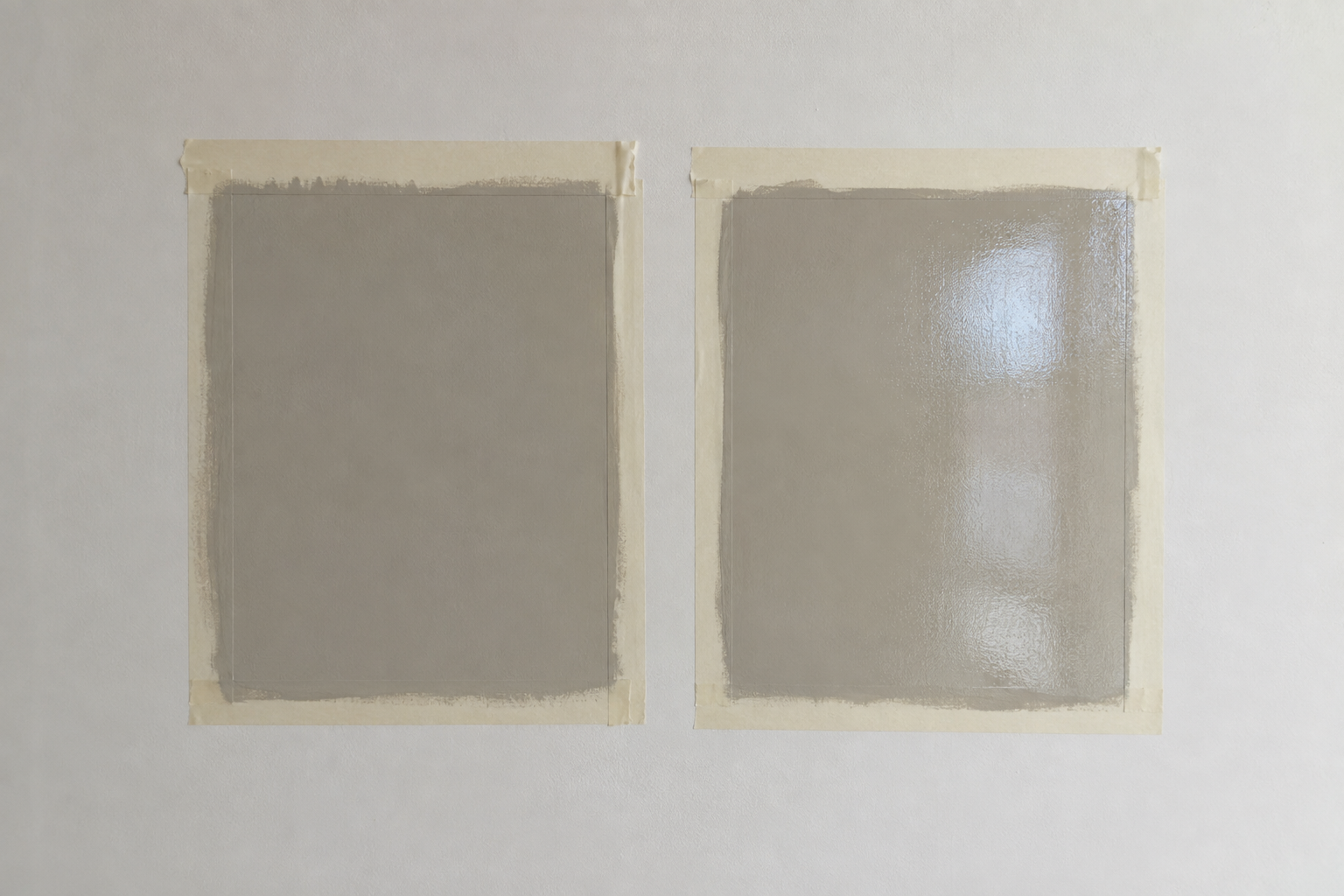Matte and glossy paint sample squares taped side by side on a wall for testing