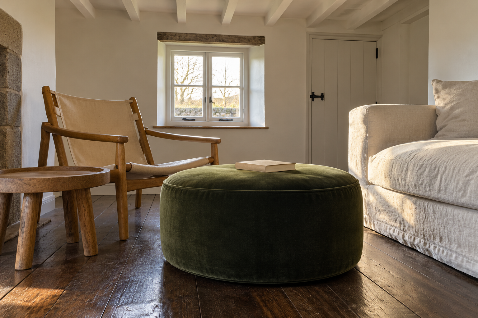 A round green velvet ottoman between a lounge chair and the end of a sofa in a low-ceilinged room.