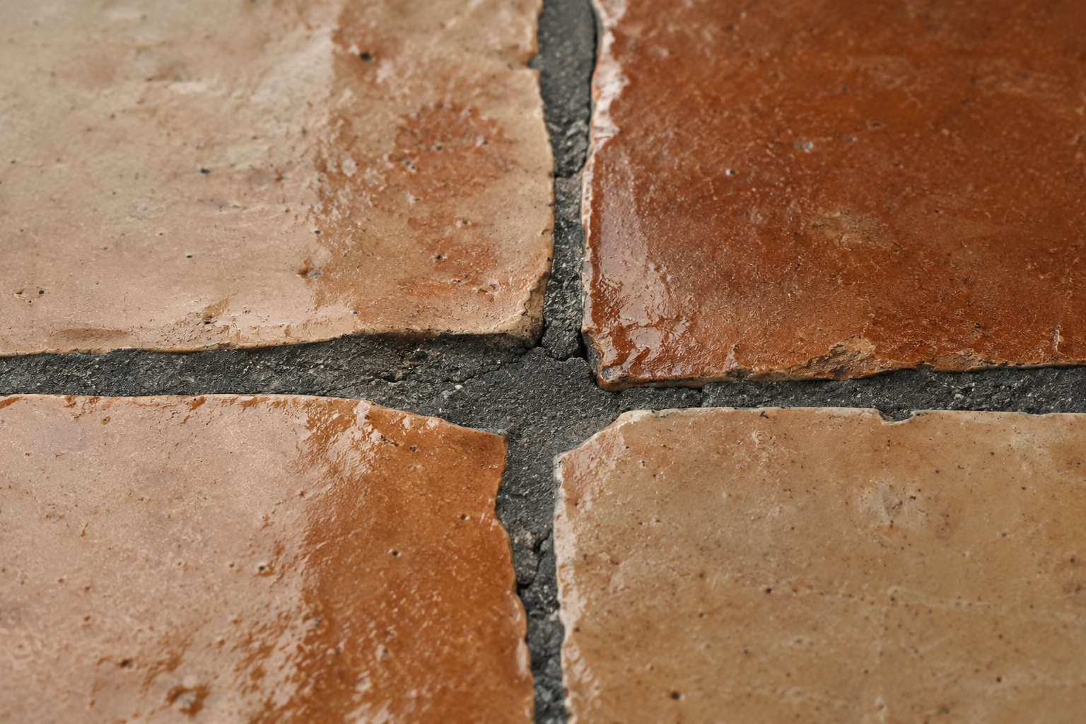 Close detail of a wide, irregular charcoal grout joint between pieces of handmade zellige tile.
