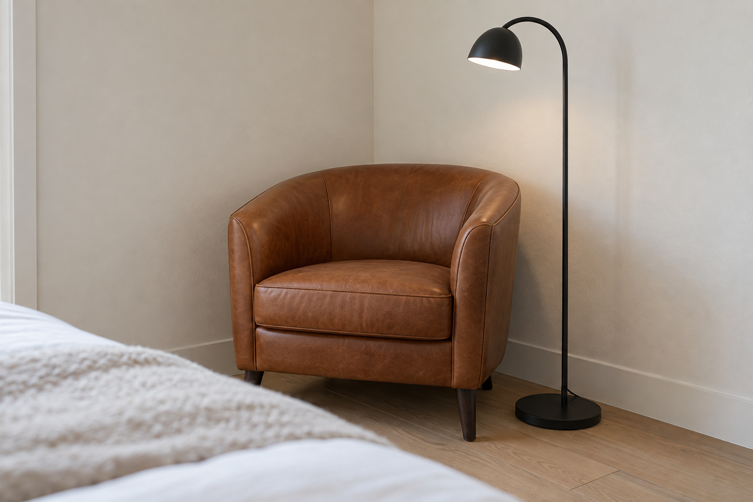 A cognac leather barrel-back reading chair with a black-steel floor lamp, fitted into a bedroom corner.