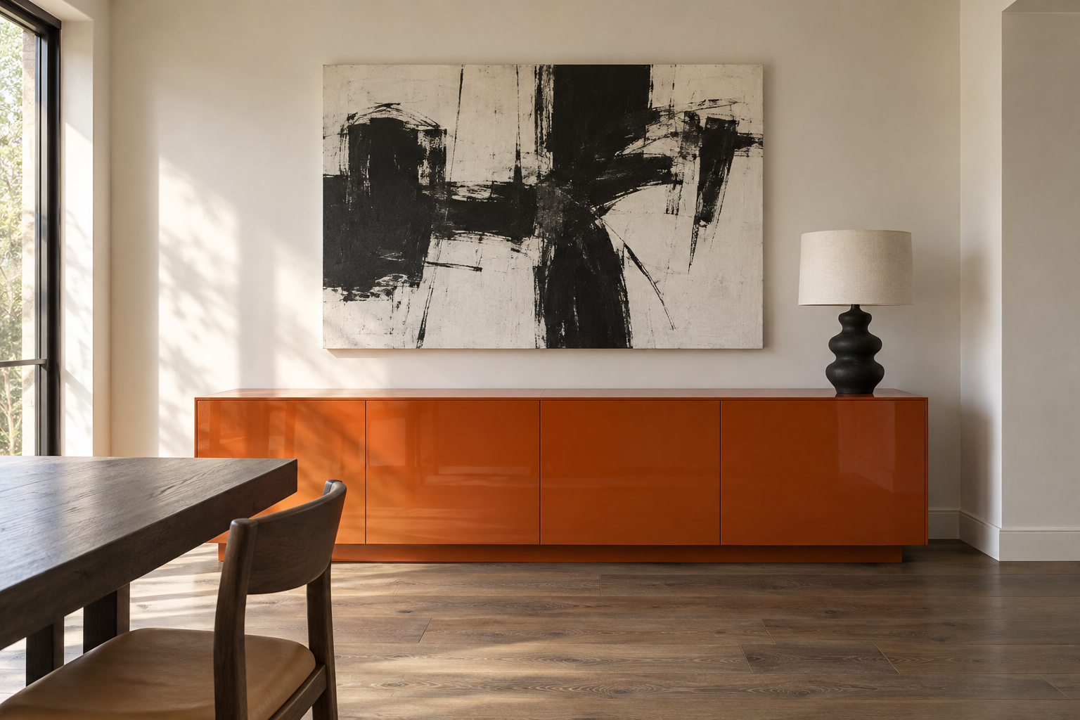 A large black and white abstract canvas hung over a long orange lacquer sideboard on a warm white plaster dining room wall.
