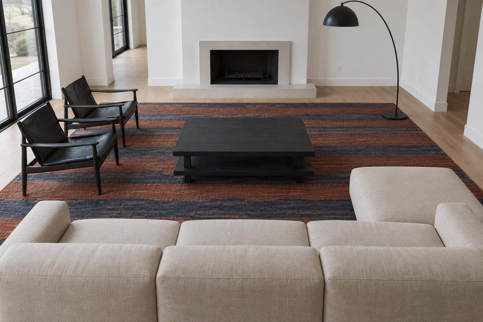 A large rust and indigo striped wool rug with the front legs of a sofa and two armchairs on it.