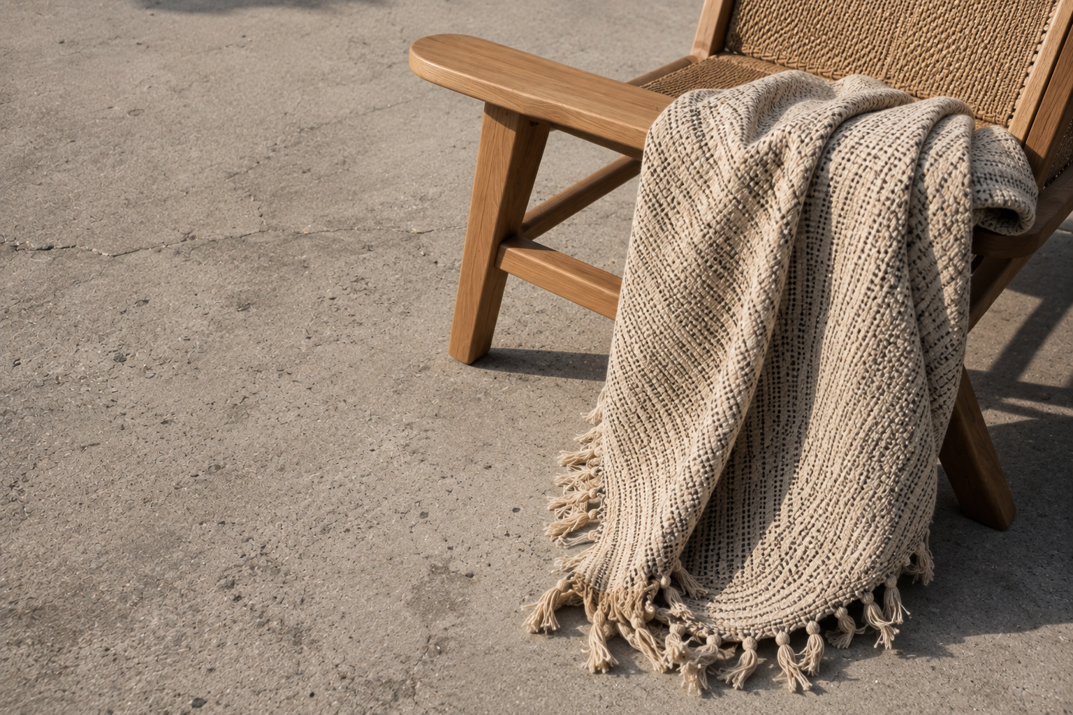 A plain concrete patio slab softened with teak furniture and a woven outdoor textile