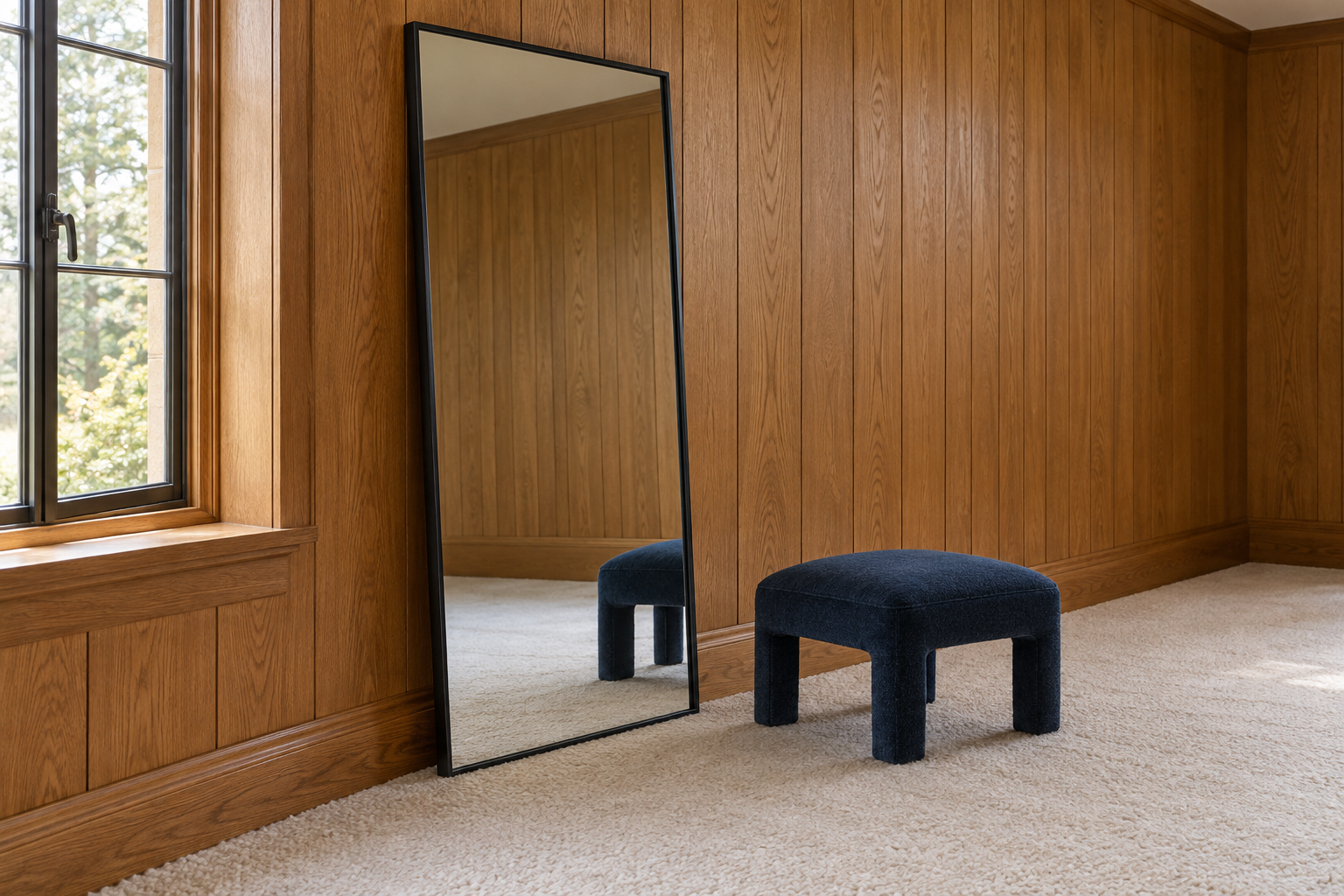 A tall black-framed floor mirror leaning beside a window in an oak-paneled bedroom.