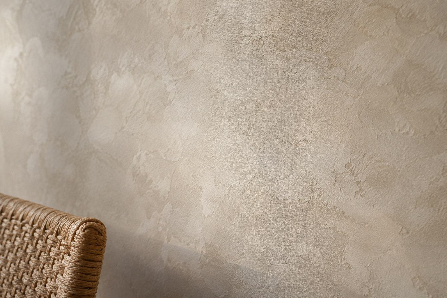 Close detail of warm oatmeal limewash plaster texture catching raking daylight, showing genuine surface variation.
