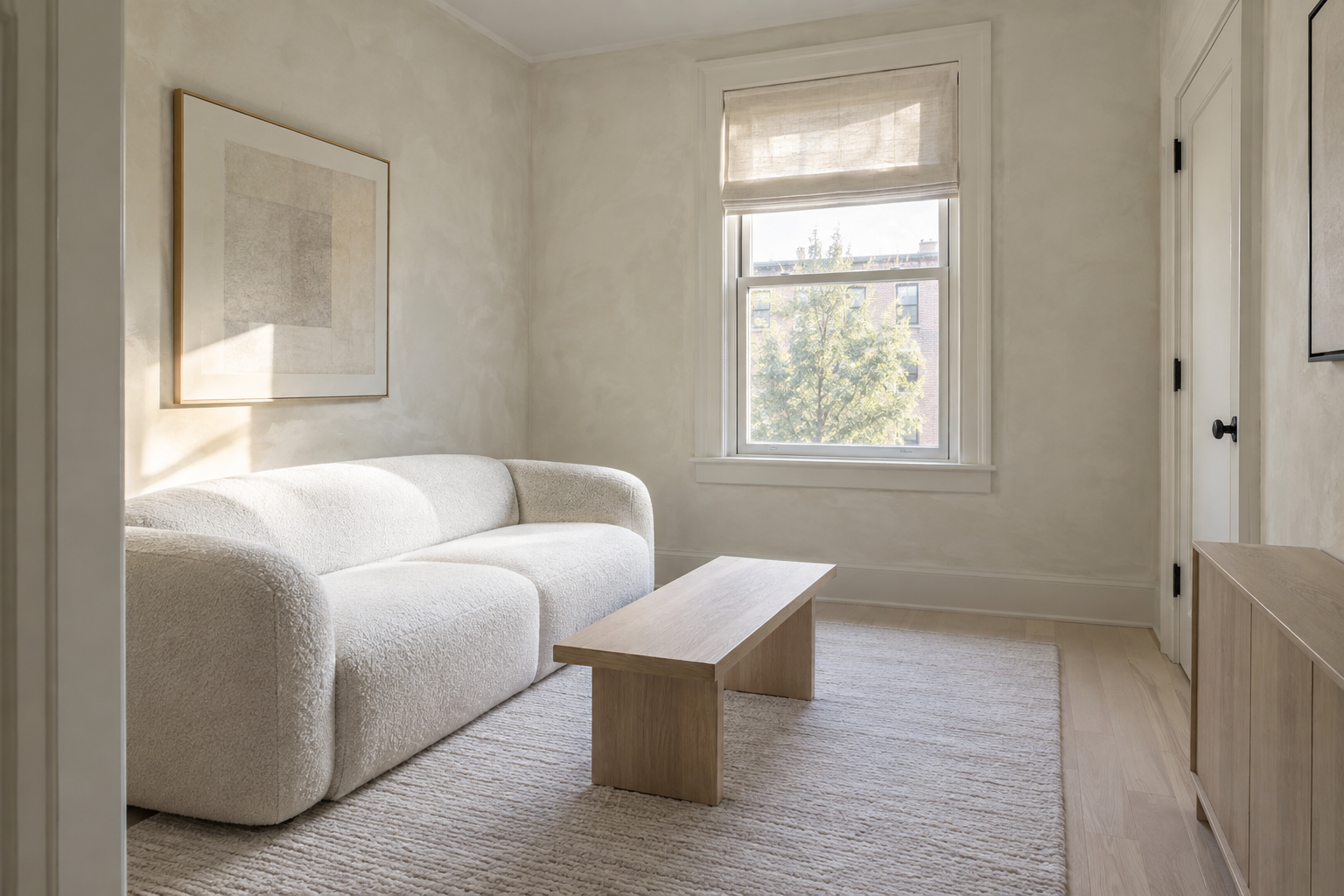 A small, pale living room with off-white furniture and limewashed plaster walls.