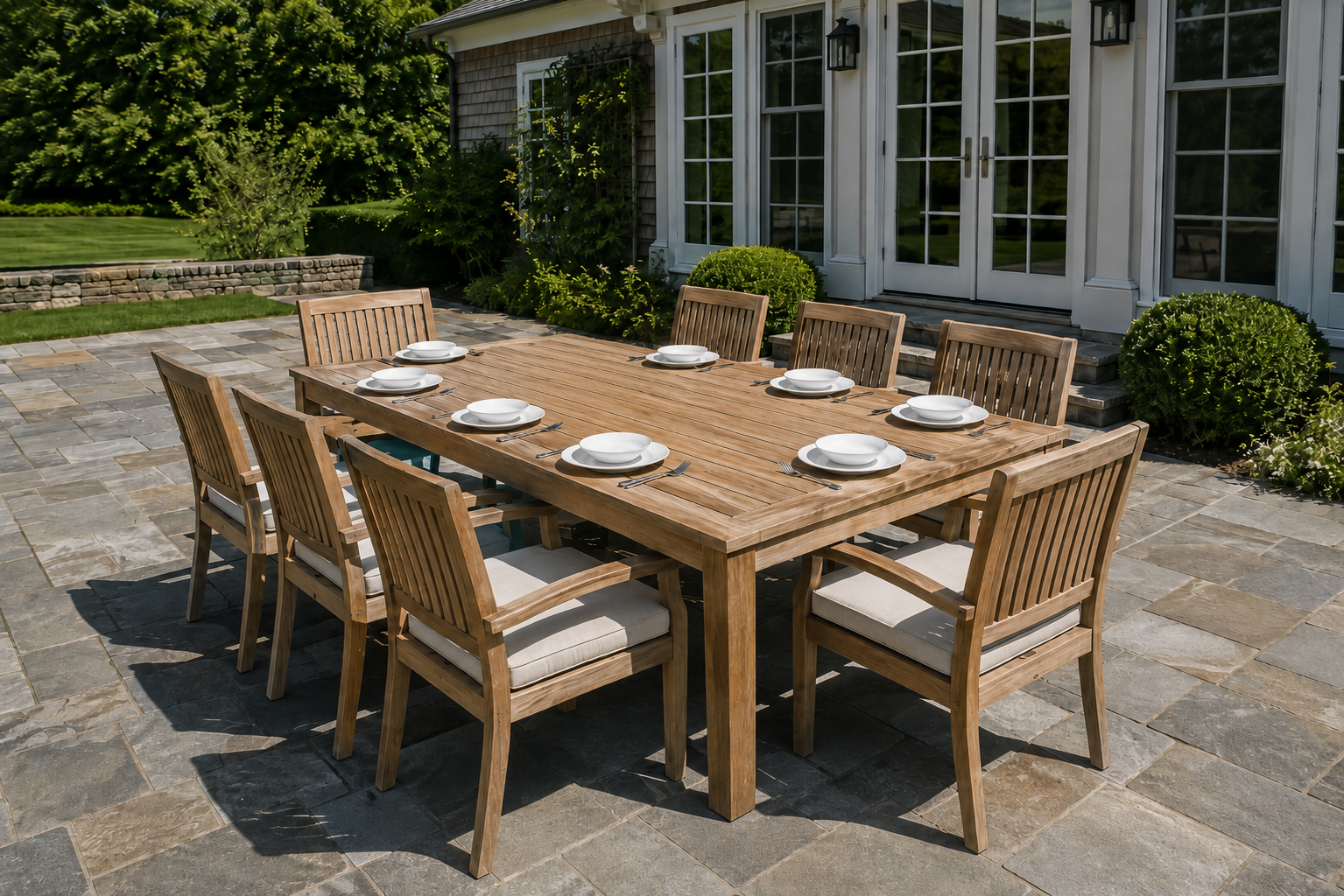 A long teak dining table with eight chairs on a large stone patio