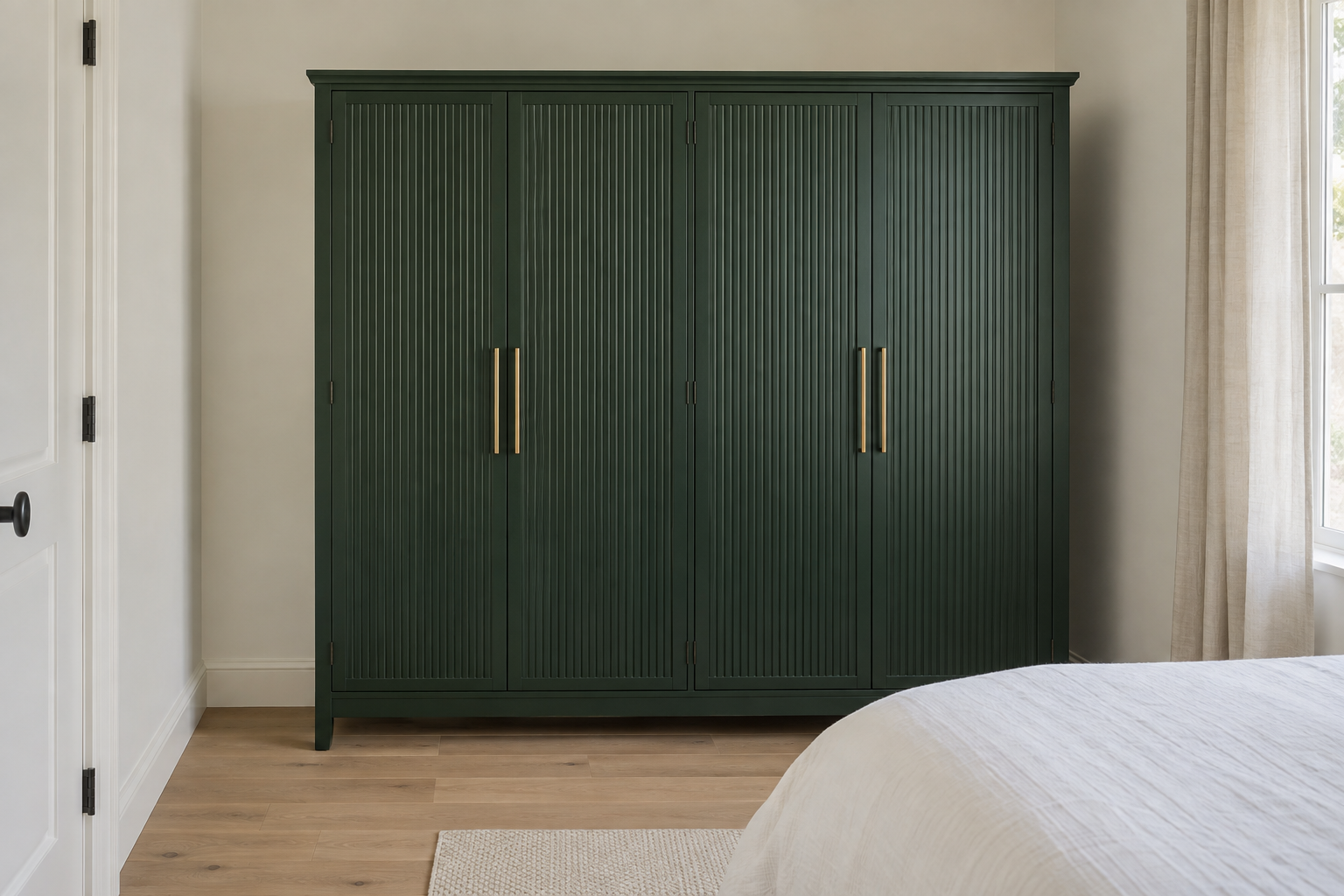 A large deep forest-green armoire with a fluted front panel design and brass pulls, filling most of one wall in a small bedroom, with a close but workable floor clearance in front of its doors.