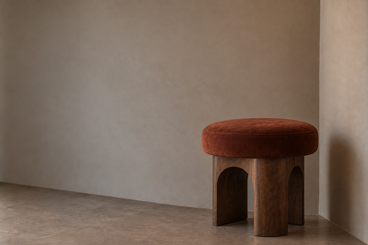 A sculptural stool with a rust suede seat styled alone in a bare, softly lit corner.