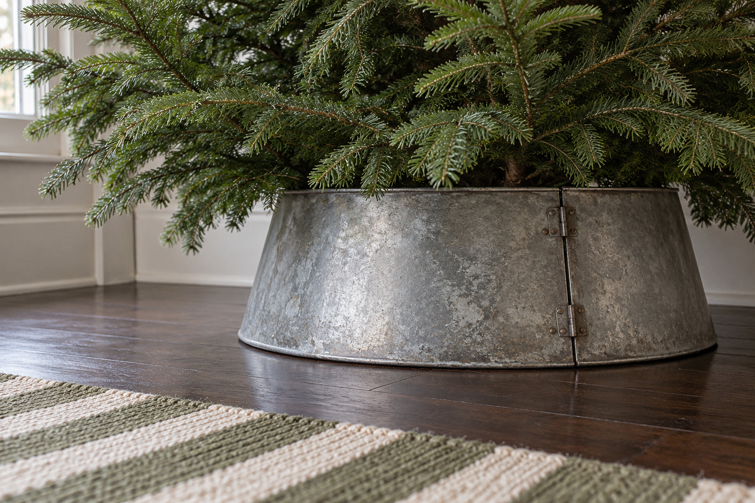 A zinc tree collar around the base of a Christmas tree on a dark oak floor.
