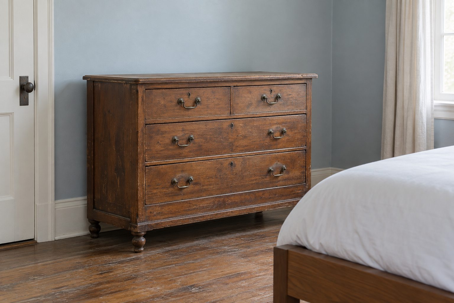 A genuinely vintage wood dresser with aged brass hardware and an uneven original finish, standing in an otherwise contemporary bedroom with a plain modern bed visible nearby.