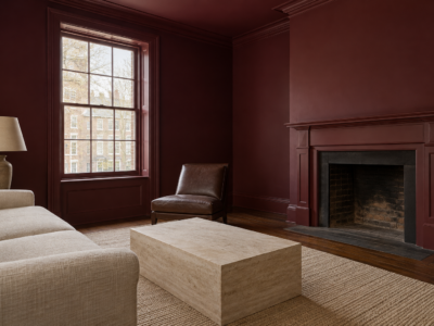 A sitting room with burgundy walls, cornice, ceiling, and window casing, and an oatmeal sofa beside a travertine table.