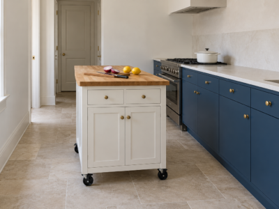 A white rolling kitchen island with a butcher-block top standing on its casters beside blue cabinets, with a cutting board and lemons on top.