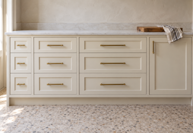 Cream Shaker kitchen drawers in three widths, each with a brass bar pull about a third as long as the drawer is wide.
