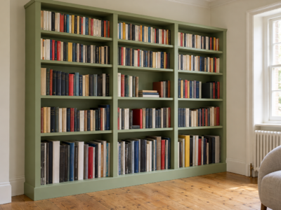 A tall bookcase painted pistachio green and filled with books, with taller shelf openings at the bottom than at the top.