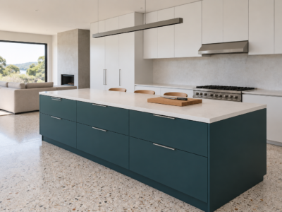 A kitchen with a deep teal island on a pale terrazzo floor, three low-backed stools on one side and a clear white top.