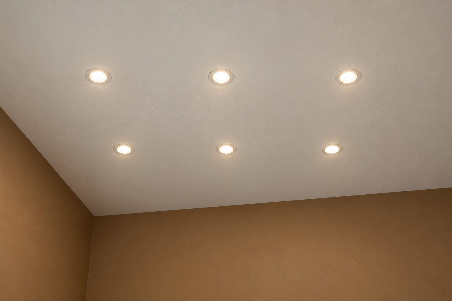 A white ceiling seen from below with six small recessed lights in two even rows, each row set in from the brown walls.