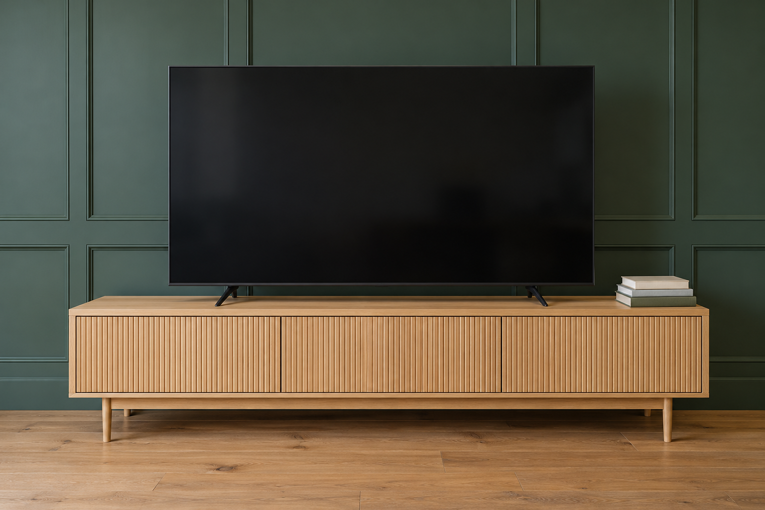 A straight-on view of a dark television on a white oak media console that extends well past the screen at each end, against a forest green panelled wall.