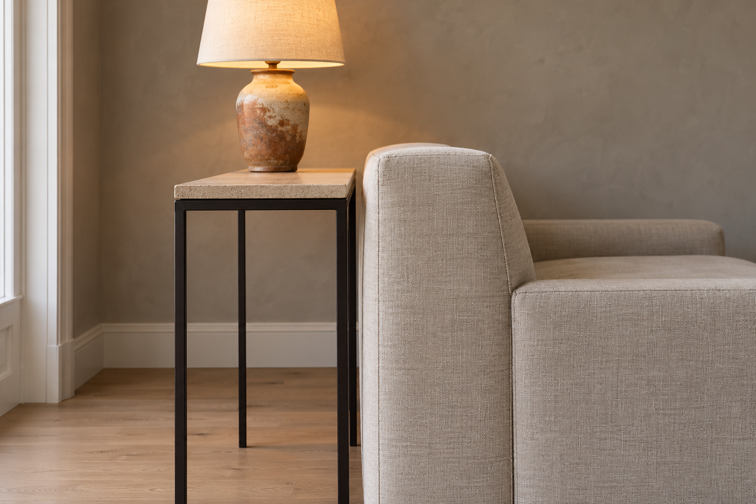 A side view of a sofa table behind a linen sofa, showing the travertine top sitting just below the top of the sofa back, with a small gap between table and sofa.
