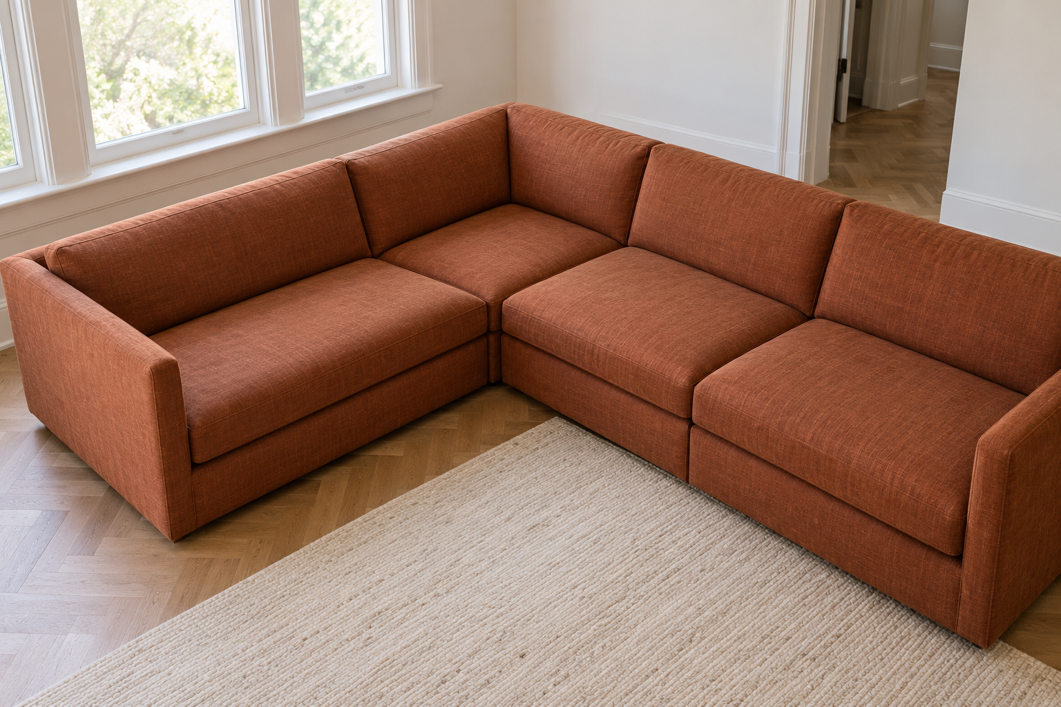 A view from above of the corner of a rust colored L-shaped sectional, showing its two sides meeting at a square corner piece and the even depth of both sides.