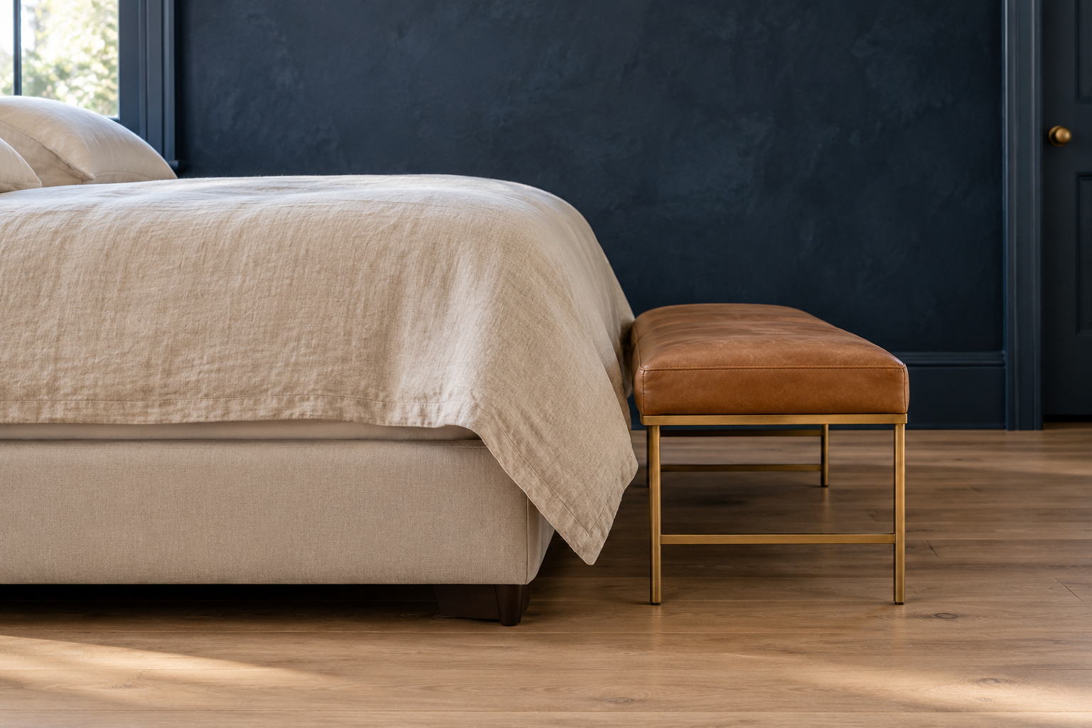 A side view of the foot of a bed and the leather bench in front of it, showing the bench seat a few inches below the top of the mattress and a small gap where the duvet hangs down.
