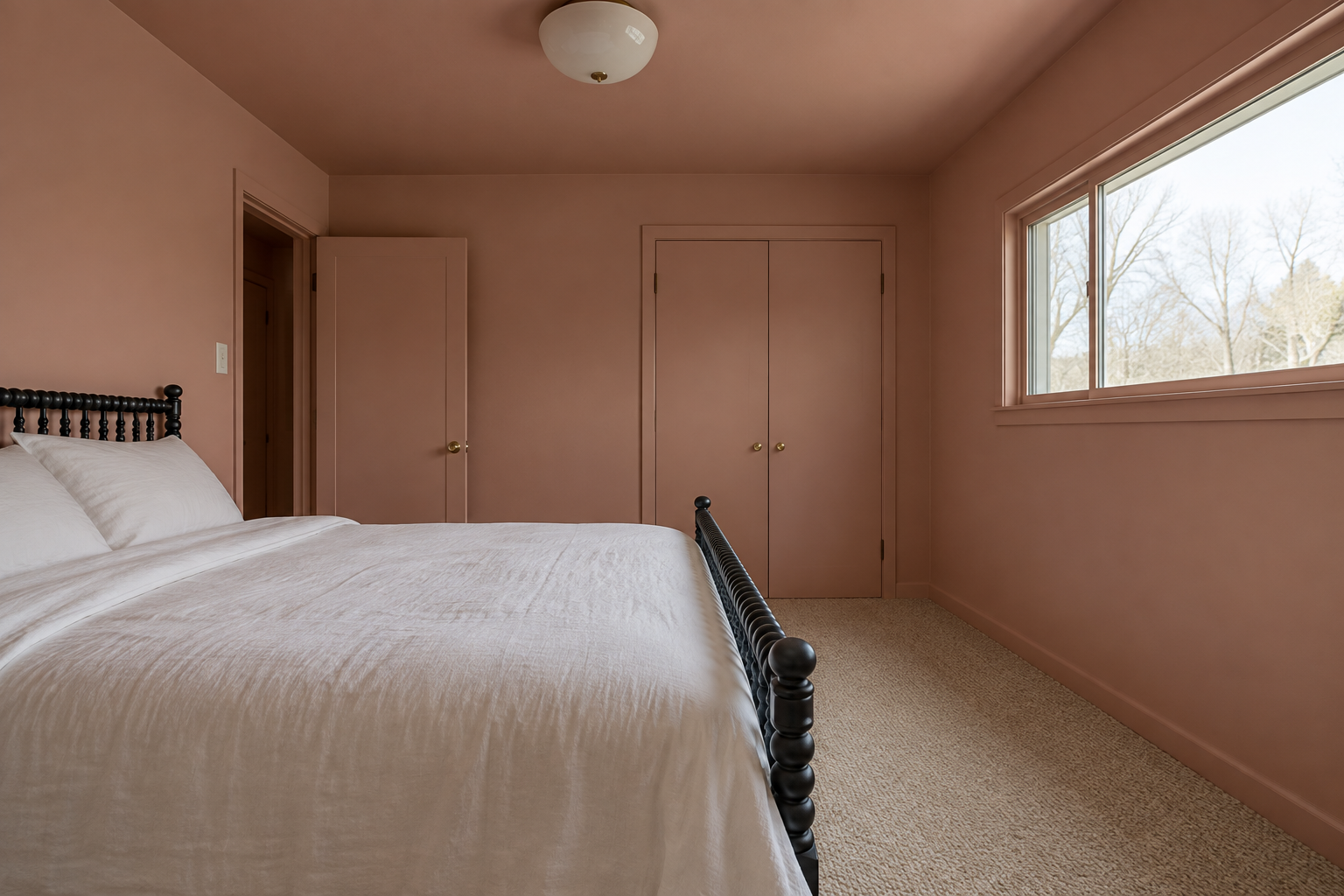 A bedroom with clay pink walls and a slightly lighter pink ceiling, with a black spindle bed under a wide window.