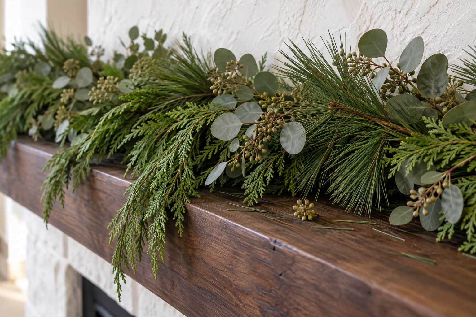 A close view of a garland of cedar, long-needled pine, and seeded eucalyptus lying on a dark wooden mantel beam.