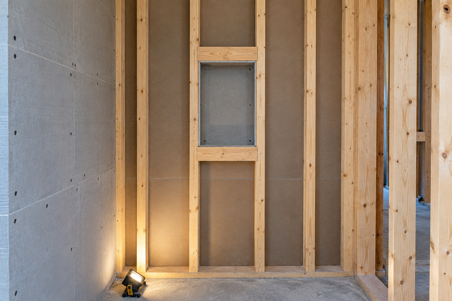 Bare wall studs in a shower under construction, with a niche framed as a box between two studs before tiling.