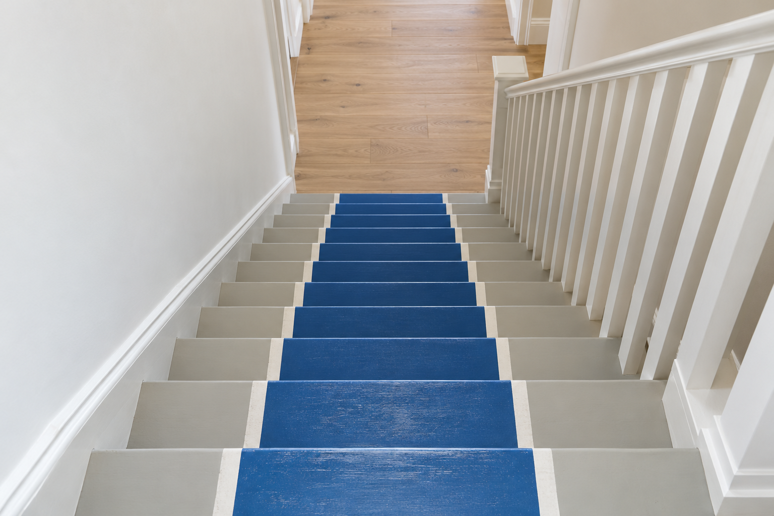 Looking down a pale gray painted staircase with a cobalt blue runner painted down the middle and thin white lines along its edges.